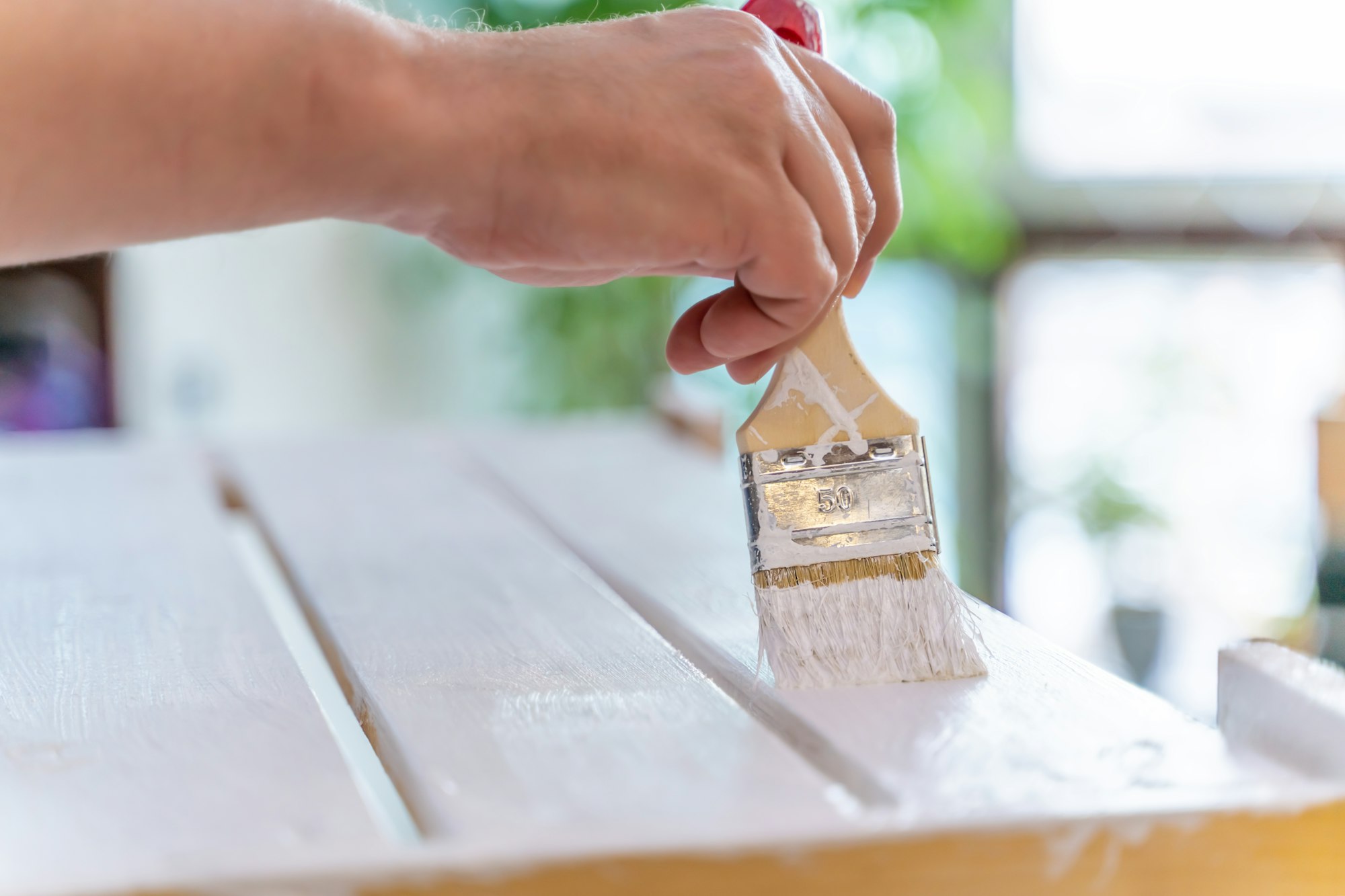 Man's hand paints wooden furniture with white paint with a brush closeup