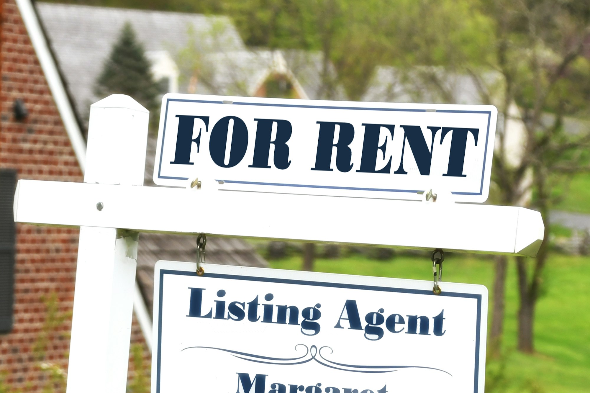 For Rent sign in front of a neighborhood with houses home in the background.